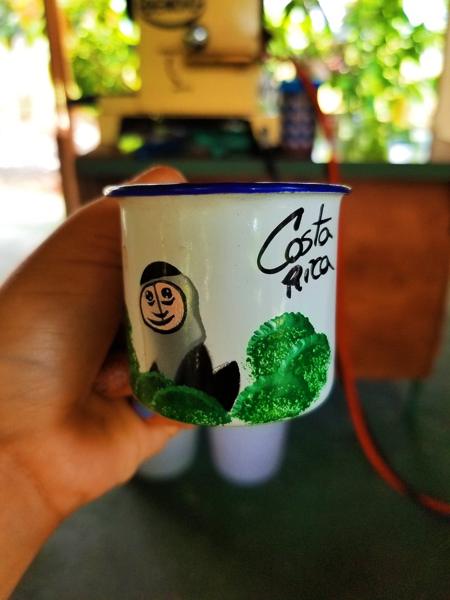 Holding a cup with an image of a monkey on a tree and 'Costa Rica' written across it. 